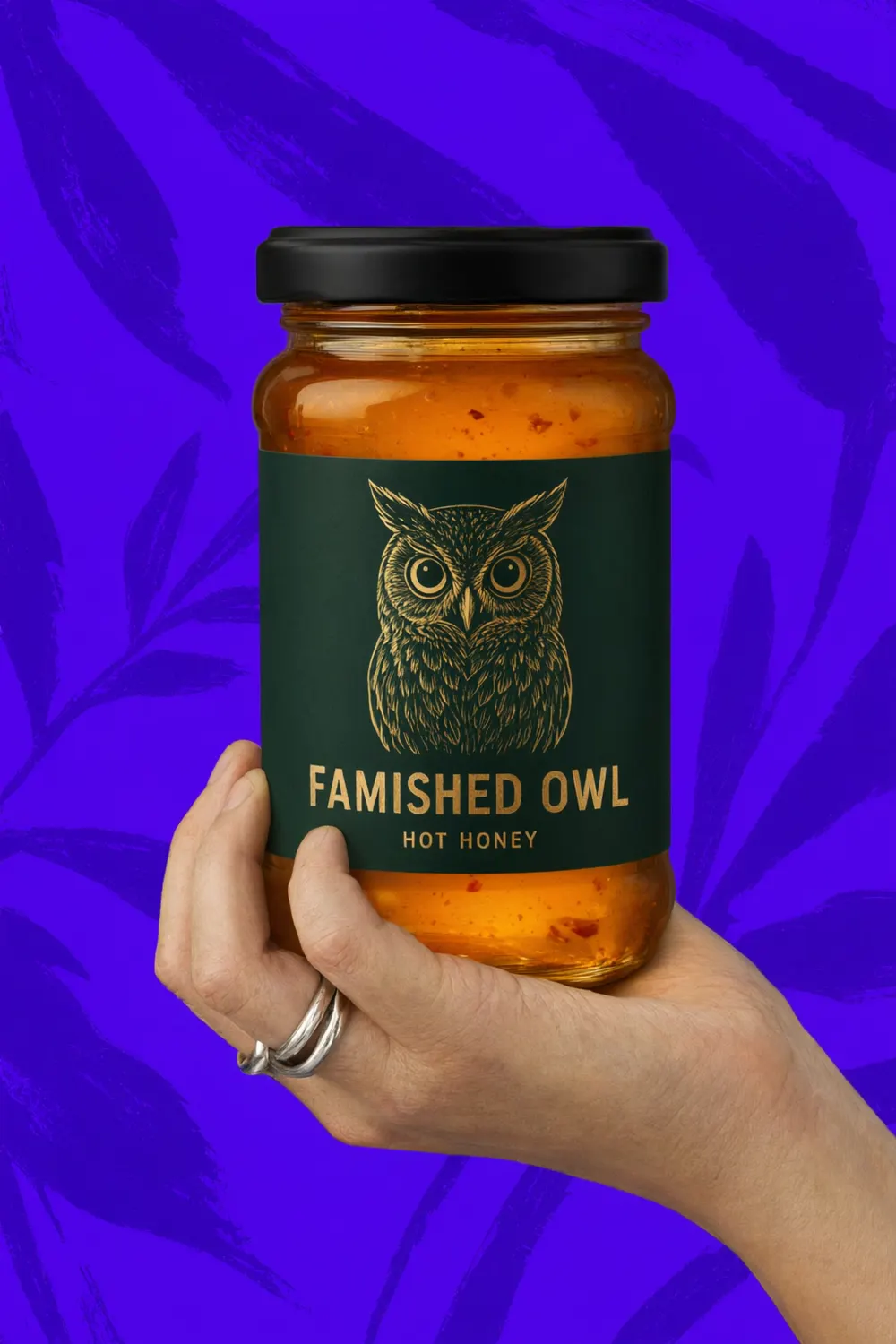 A hand holding a jar of Famished Owl hot honey